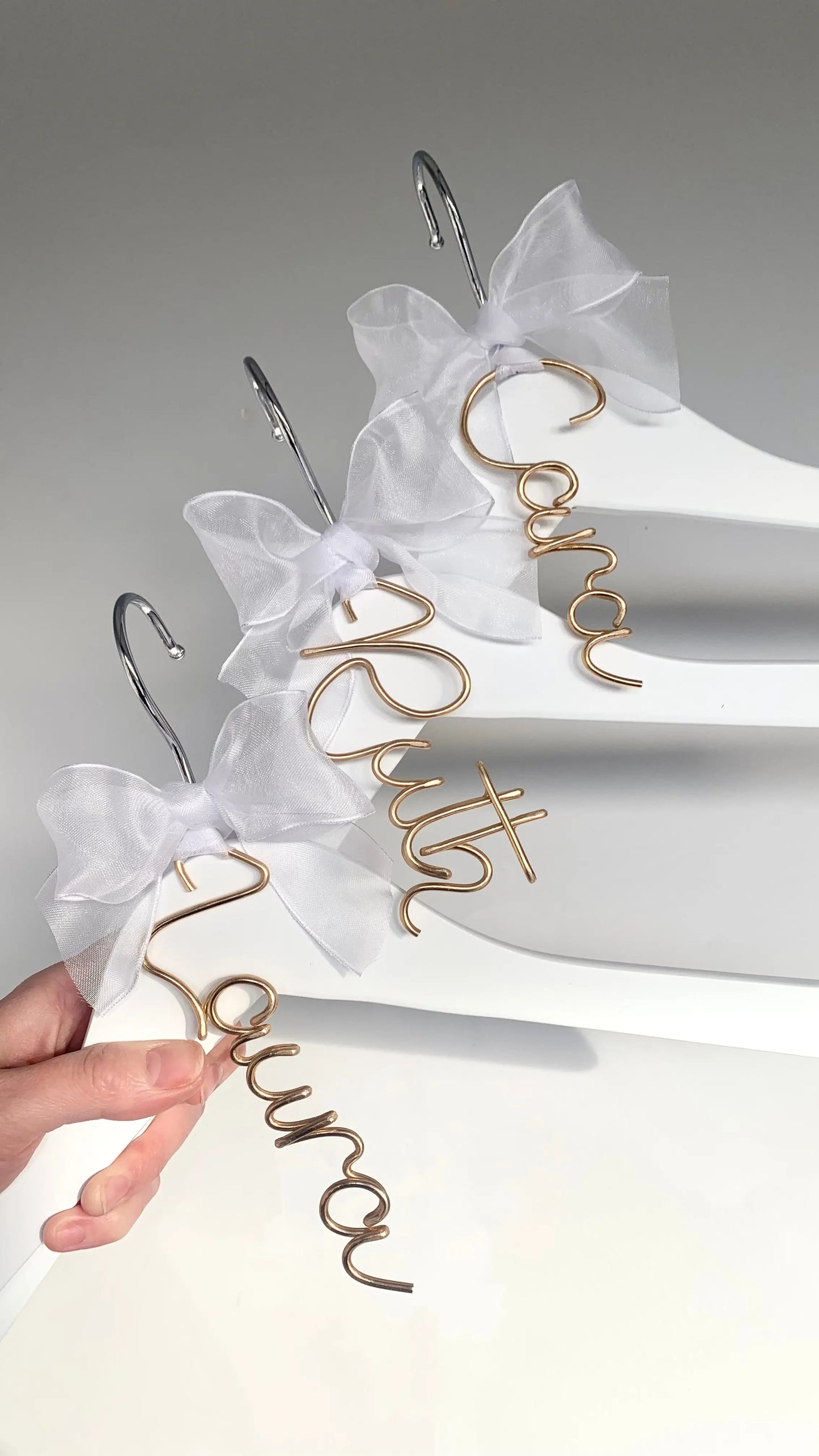 set of wire hanger name charms for bridesmaids, on white dress hangers, with white organza bows