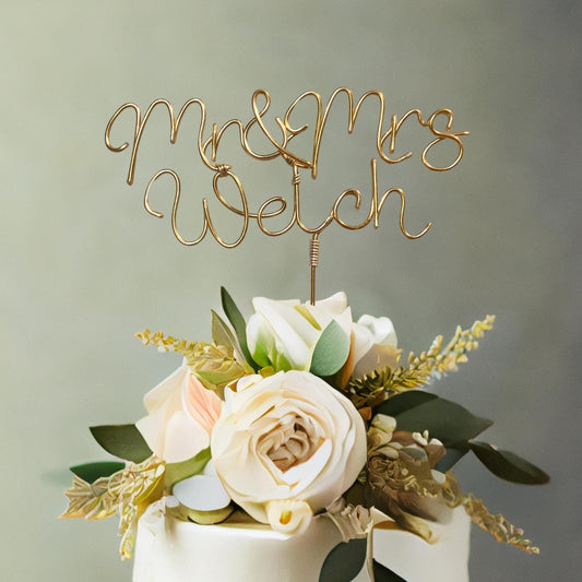 mr and mrs personalised wire wedding cake topper, in bronze gold wire, on top of wedding cake with large floral arrangement