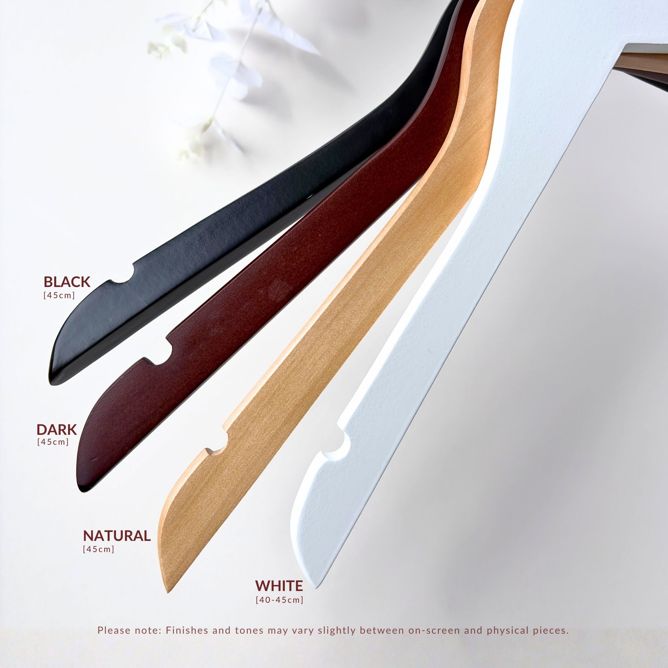 Set of four wooden hangers in black, dark brown, natural, and white on a light gray background.