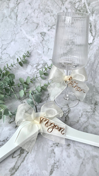 Ivory organza bow charm, with bronze gold name, on both a wine glass and bridesmaid hanger