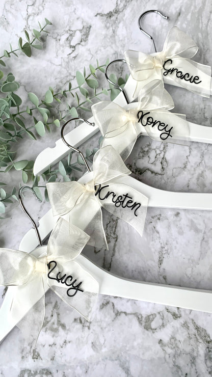 Ivory organza bow charms, with black wire names, on white hangers