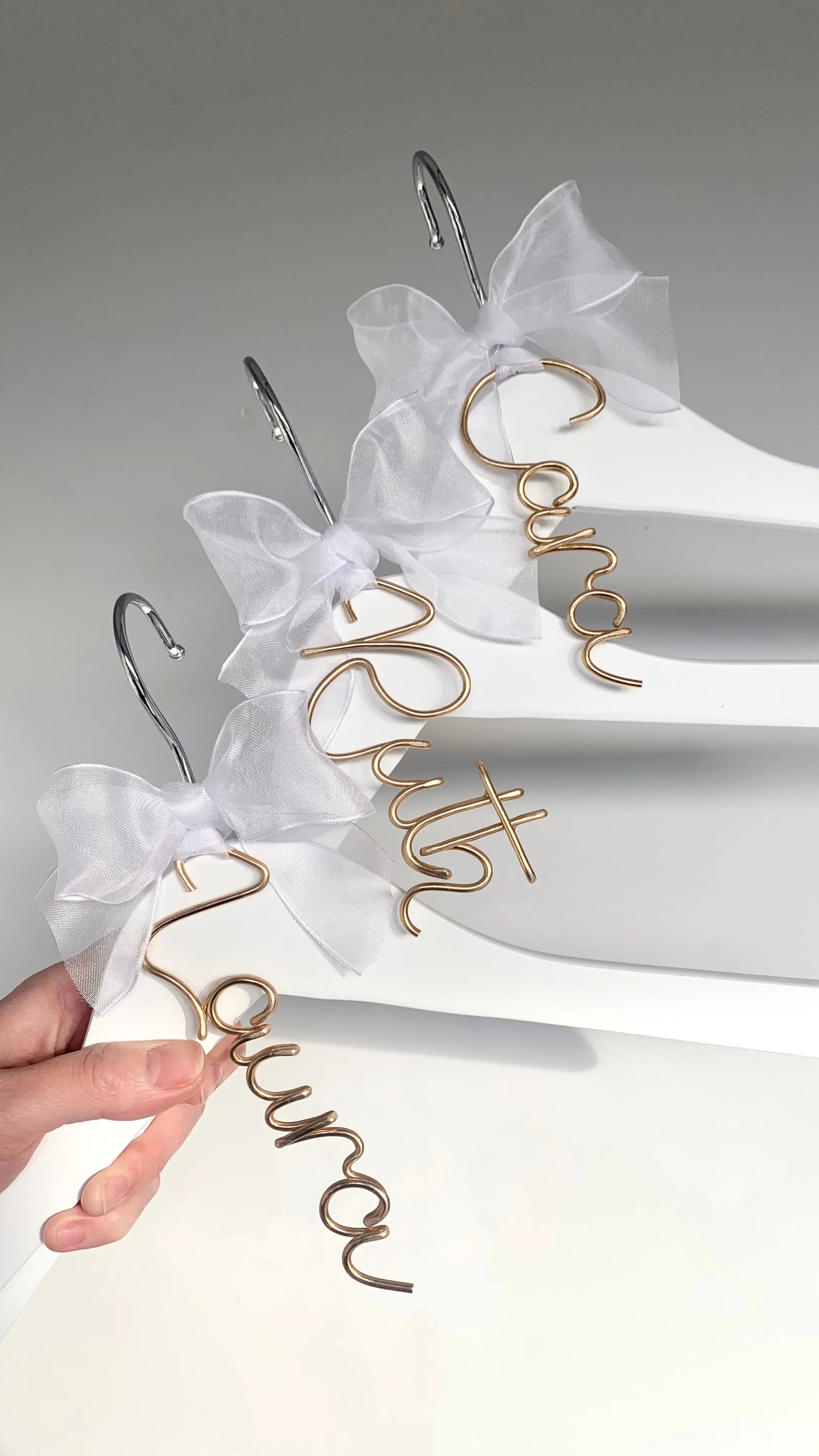 set of wire hanger name charms for bridesmaids, on white dress hangers, with white organza bows