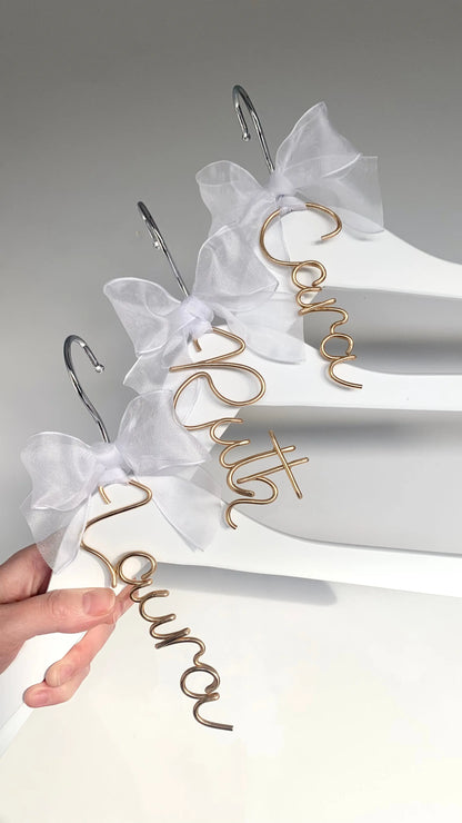 set of wire hanger name charms for bridesmaids, on white dress hangers, with white organza bows