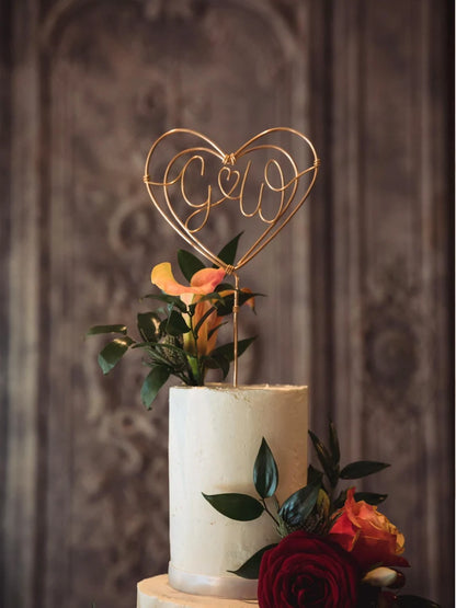 copper heart cake topper, on top of white buttercream iced wedding cake with rich autumnal floral arrangements of red roses and deep orange flowers
