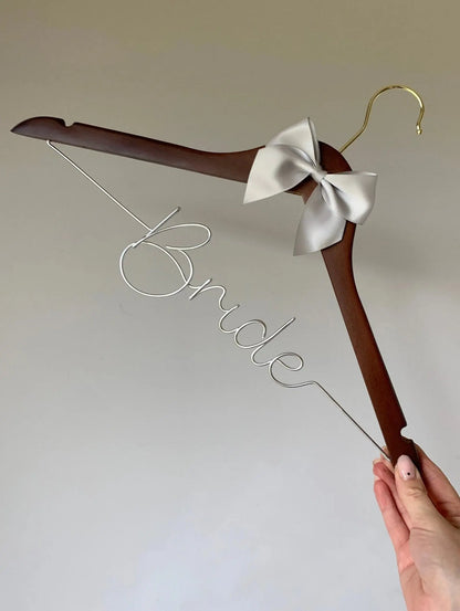 a dark wood hanger, with silver wire lettering reading ‘Bride’, and satin silver bow