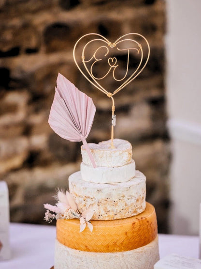 wire heart wedding cake topper with couple’s initials, handmade, on top of a cheese wheel wedding cake