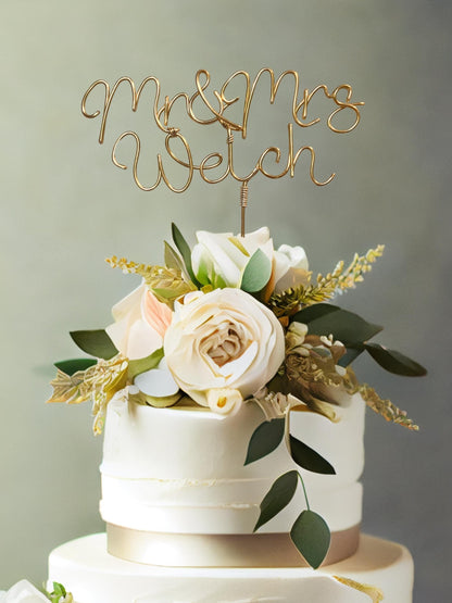 mr and mrs personalised wire wedding cake topper, in bronze gold wire, on top of wedding cake with large floral arrangement