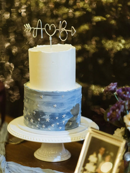 personalised arrow cake topper, in silver wire, on top of wedding cake with white and blue tones and star decorations